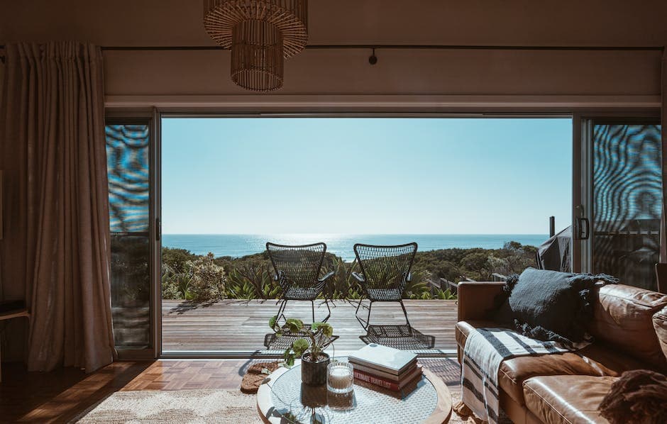 Interior design of luxurious apartment in a timeshare with large balcony doors and wooden terrace having picturesque view on green forested seashore and calm blue sea
