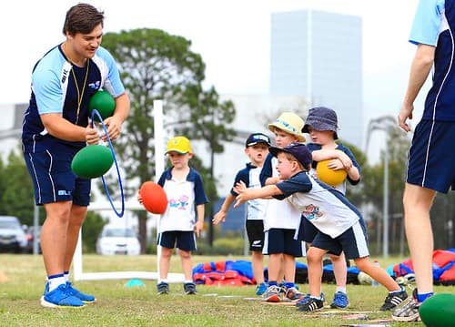 a group of young children are sporting on a field with a teacher/coach